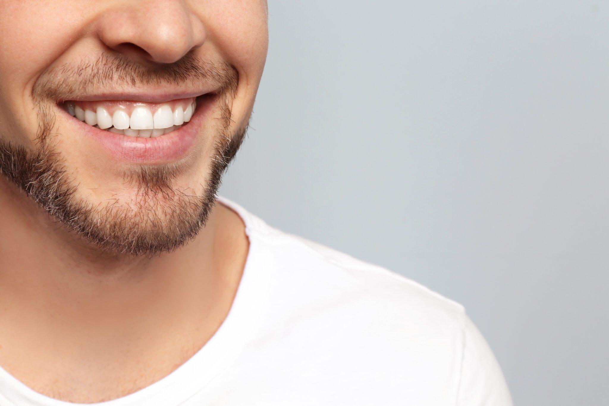 Young man with beautiful smile on grey background. Teeth whiteni smiling man - Ideal Image Dentistry