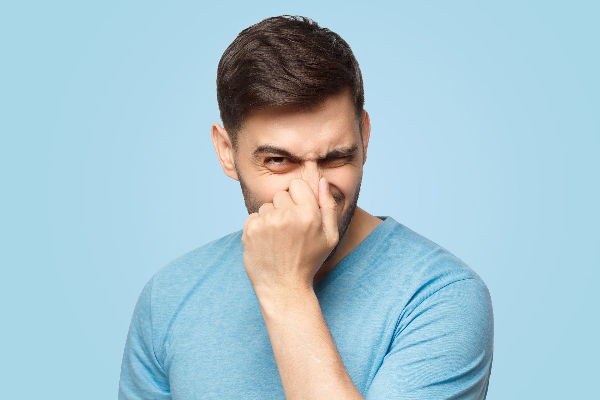 The true causes of bad breath and how to prevent it man holding nose - Ideal Image Dentistry