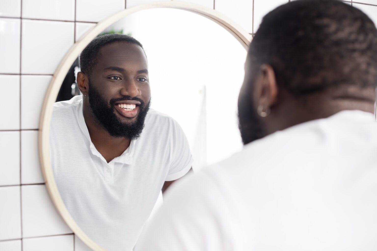 A smiling man looking in a mirror.
