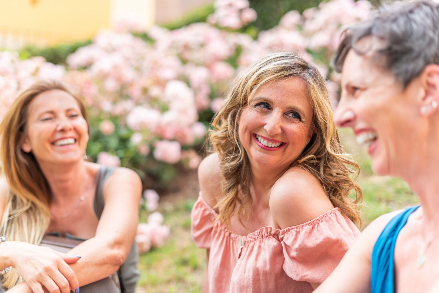 Three adult women sitting in the park laughing and chatting.